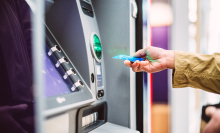 Female hand inserting bank card into automatic cash machine (ATM) to access bank account services in the city. Cash withdrawing, paying bills, checking account balance, transferring money, currency exchange at ATM. Self-service concept.