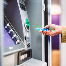 Female hand inserting bank card into automatic cash machine (ATM) to access bank account services in the city. Cash withdrawing, paying bills, checking account balance, transferring money, currency exchange at ATM. Self-service concept.