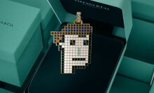 A piece of jewellery in the shape of a pixellated face hangs in front of a green Tiffany box.