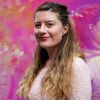 An image of journalist and author Rachel Thompson on a pink backdrop. She has long brown hair and is wearing a light pink dress. 