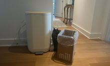 Mill composter bin, cardboard box, and cat with hallway and table in background