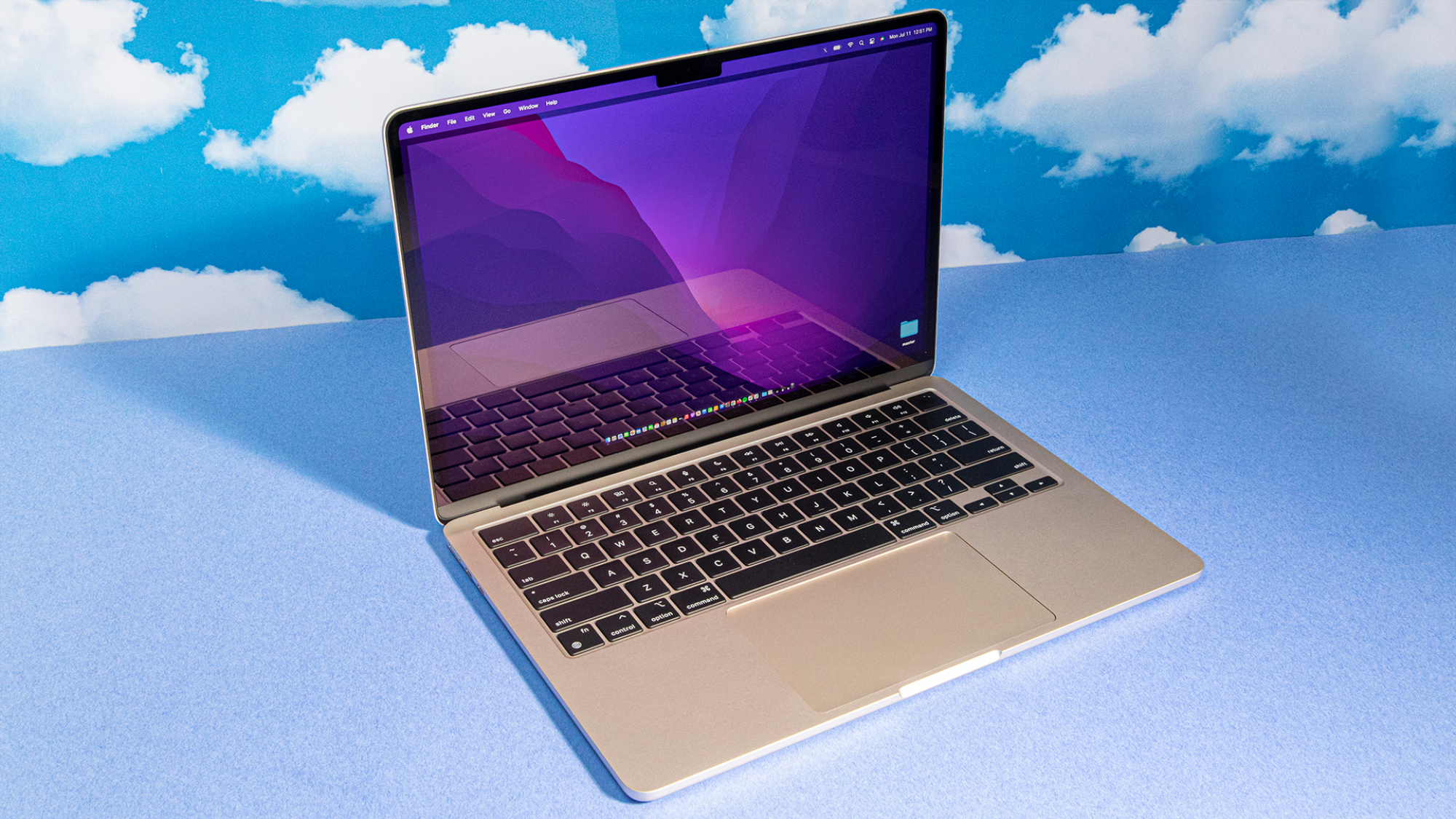 2022 M2 MacBook Air open and in profile view against a blue backdrop with repeated cloud patterns