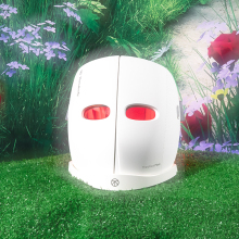 white mask with red LED light shining through eye holes against grass and flower background