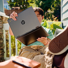 a teenage boy holding up an hp chromebook x360 and putting his legs up while sitting out on a sunny porch