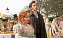 A man and woman in old fashioned, fancy clothing stand in the street.