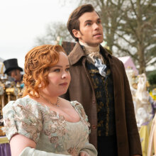 A man and woman in old fashioned, fancy clothing stand in the street.