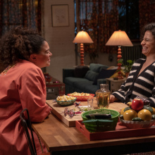 Still from 'Babes' shows Ilana Glazer and Michelle Buteau's characters laughing and sharing snacks.