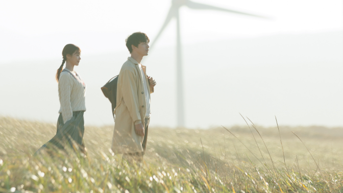 A still from 'Beyond Goodbye' of a man and woman in a field, with wind turbines in the background.