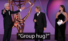 Two men and a woman stand on an awards show stage.