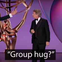 Two men and a woman stand on an awards show stage.