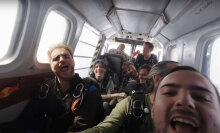 A group of skydivers on an airplane smile and laugh at the camera.