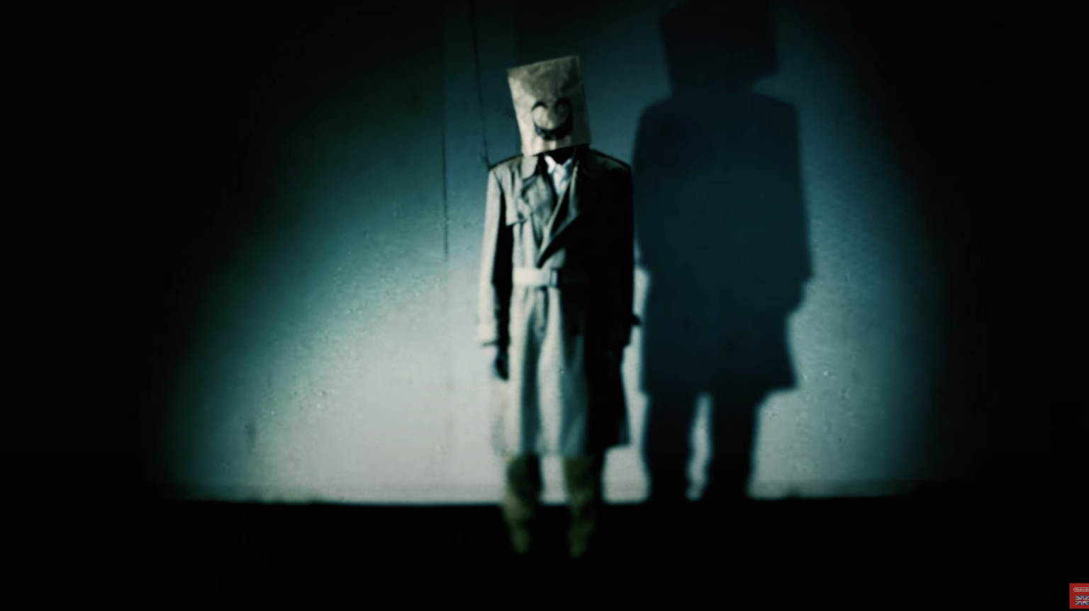 A creepy still from "Emio" showing a person with a bag over their head emblazoned with a smile.