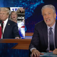 A man in a suit sits behind a talk show desk making a face. In the top left is an image of Donald Trump.