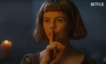 A woman holds a finger to her lips.