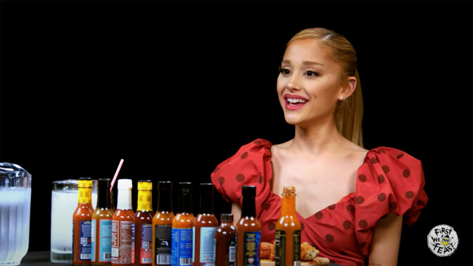 A woman sits in front of a table covered with hot sauce.