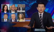 A man in a suit sits behind a talk show desk, with images of six other people in the top left.