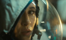 A female astronaut is seen up close, wearing a space suit.