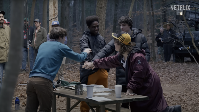 On set for "Stranger Things," four boys put their hands together.