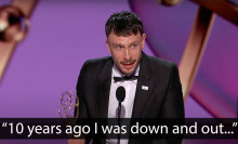 A man in a suit stands on a stage, holding an award.