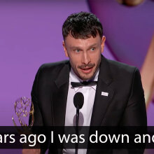 A man in a suit stands on a stage, holding an award.