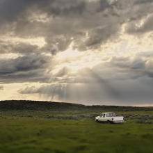 A truck drives through New Mexico with the sun shining through the clouds.