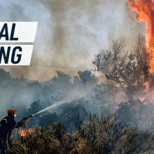 A firefighter tries to put down a raging fire. Caption reads "global boiling"