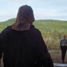A masked killer approaches a woman in the wilderness.