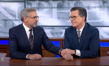 Two men in suits sit behind a desk, looking at each other with affection.