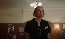 A woman stands in a hotel reception looking afraid.