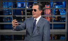 A man in a suit and sunglasses stares at a smartphone.