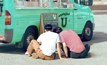 Two men sitting next to each other in front of a coffee truck. Their backs are to the viewer.