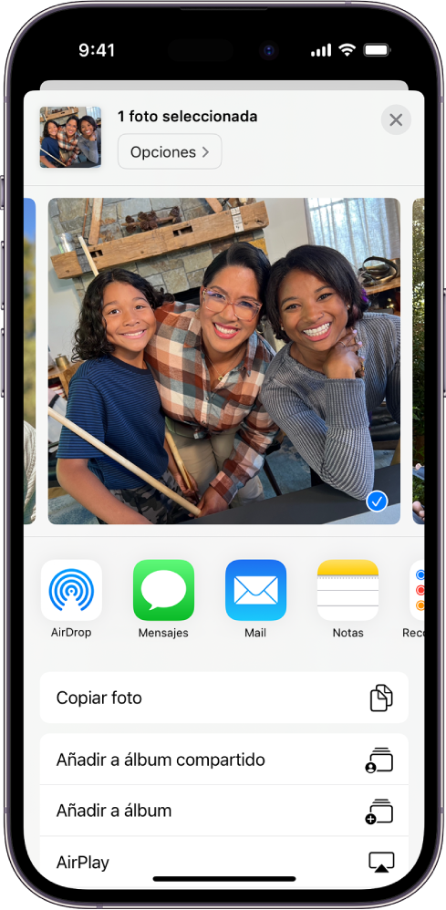 Se muestra una foto seleccionada en la mitad superior de la pantalla del iPhone, con las opciones para compartir debajo: AirDrop, Mensajes, Mail y Notas. Debajo de estas opciones para compartir hay otras acciones que se pueden realizar a la foto, como “Copiar foto”, “Añadir a álbum compartido”, “Añadir a álbum” y AirPlay.