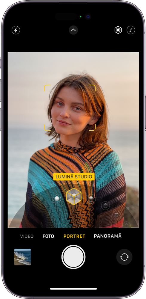 Ecranul Cameră în modul Portret; în vizor, subiectul este clar, iar fundalul este estompat. Discul pentru selectarea efectelor de Iluminare portret este deschis în partea de jos a cadrului și este selectată opțiunea Lumină studio. În partea din stânga sus a ecranului este butonul Bliț, în centru sus este butonul Comenzi cameră, iar în dreapta sus se află butoanele pentru ajustarea intensității pentru Iluminare portret și Control adâncime. În partea de jos a ecranului, de la stânga la dreapta, se află butonul Vizualizator foto și video, butonul Fotografiați și butonul Selector cameră - orientată în spate.