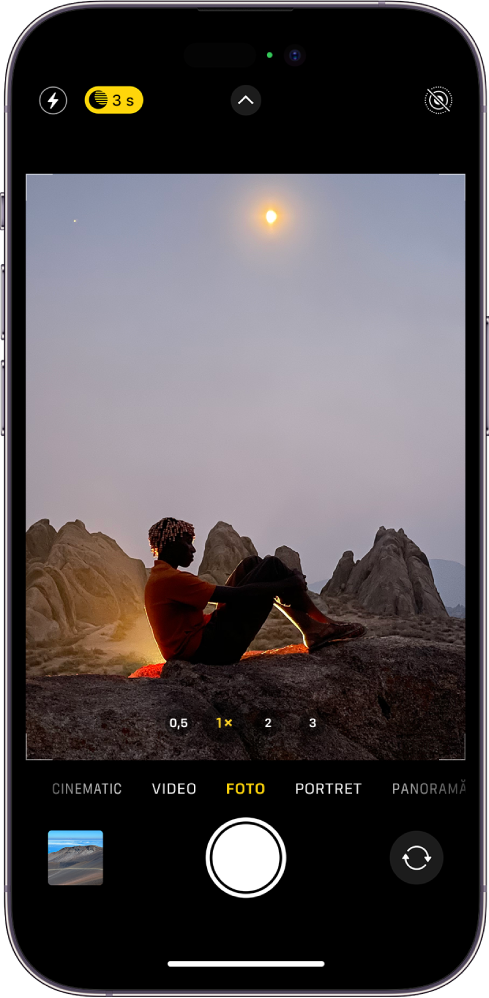 Ecranul Cameră în modul Foto. Butoanele pentru bliț și modul nocturn apar în colțul din stânga sus al ecranului și modul Noapte este activat. Butonul Comenzi cameră se află în centru sus, iar butonul Live Photo se află în colțul din dreapta sus. În partea de jos a ecranului, de la stânga la dreapta, se află butonul Vizualizator foto și video, butonul Fotografiați și butonul Selector cameră - orientată în spate. În cadrul camerei se află o scenă de noapte.