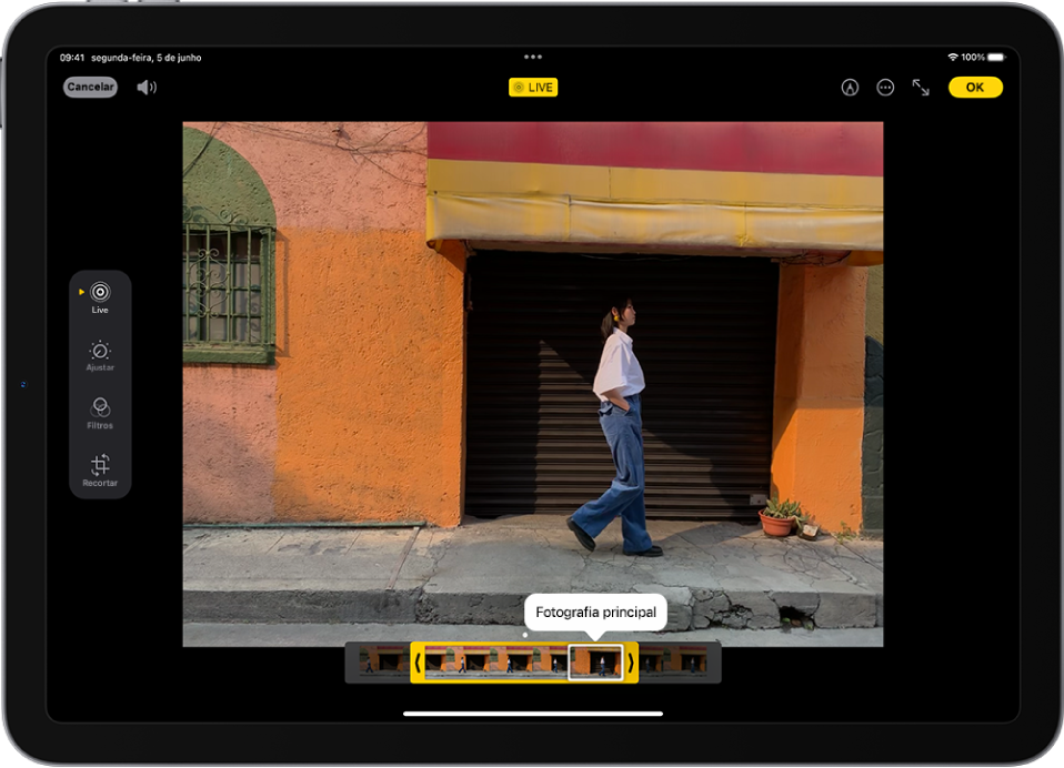 Uma Live Photo encontra‑se ao centro do ecrã de edição na aplicação Fotografias. O visualizador de fotogramas encontra-se ao longo da parte inferior do vídeo e há um contorno amarelo em redor dos fotogramas selecionados para incluir na Live Photo editada; está selecionada um único fotograma para criar a fotografia principal. As ferramentas de edição encontram-se no lado esquerdo do ecrã; de cima para baixo: Live Photo, Ajustar, Filtros e Recortar. Live Photo está selecionado.