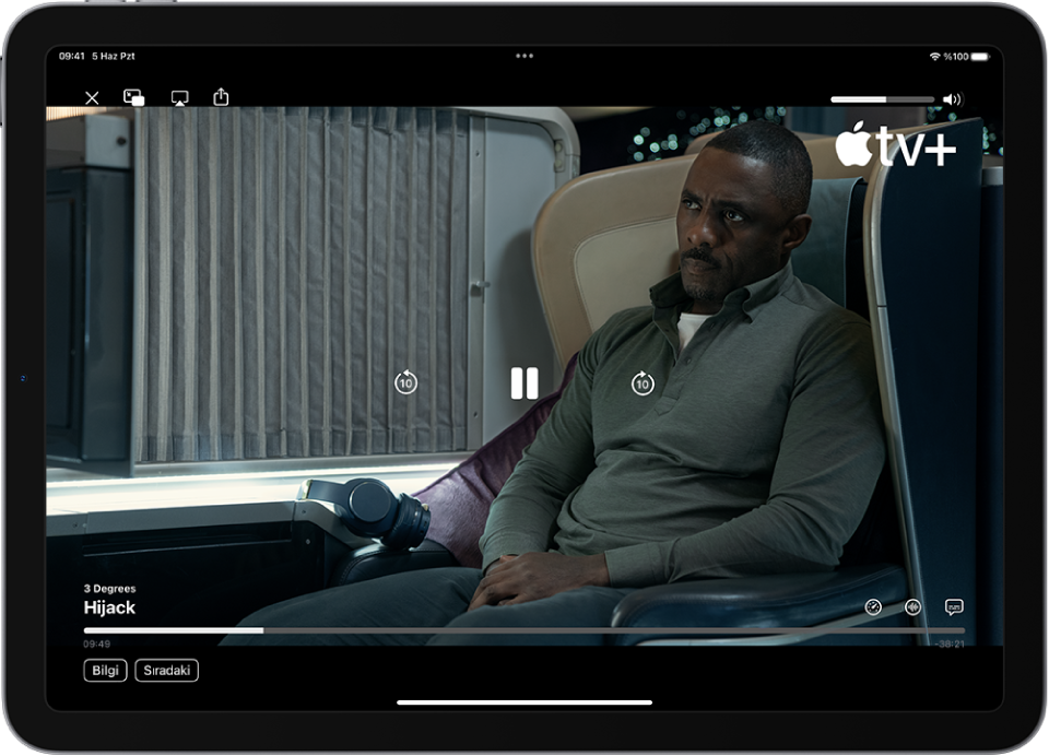 Bir TV şovu oynatılıyor; denetimler görünür durumda. Kapat, Resim İçinde Resim, AirPlay ve Paylaş düğmeleri sol üstte. Ses yüksekliği sürgüsü sağ üstte. Ortada; 10 saniye geriye atlama, duraklatma ve 10 saniye ileriye atlama düğmeleri var. Alt orta tarafta, video konumunu ayarlamak için sürükleyebileceğiniz bir sürgü var; sürgünün yanlarında geçen süre ve kalan süre görünüyor. Sağ altta oynatma hızını değiştirme, dil ve altyazı ekleme düğmeleri var. Sol altta içeriğin açıklamasını görüntüleme ve içerikleri Sıradaki’nde görüntüleme düğmeleri var.