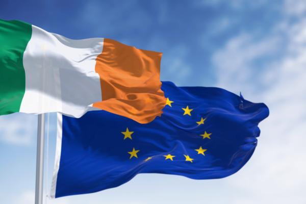 Against a clear blue sky, we see the flag of the Republic of Ireland and the flag of the EU.
