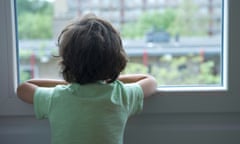 A boy resting his arms on a window frame looks out at an urban area