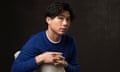 Sean Wang, wearing a white T-shirt under a blue jumper, sits sideways on a chair, hands linked, facing the camera