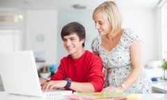 A mother looks over her son's shoulder as he works on the laptop.