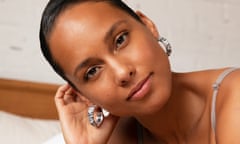 Alicia Keys smiling for the camera wearing a vest and silver earrings