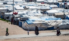 Women and children walk past several rows of tents in Roj, Syria