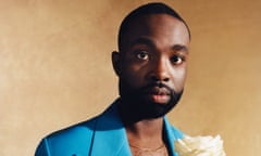 crop of a portrait of Paapa Esseidu wearing a sky blue jacket and holding a long-stemmed white rose