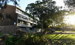 A three storey row of flats with garden beds and some mature trees in view