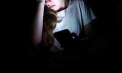 Woman sitting in the dark looks at her smartphone.