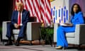 a man in a suit and tie appears to rant on stage while a woman in a blue suit holding papers looks off to the side