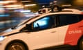 A bright, nighttime close-up of a white and orange self-driving care with no one in the driver's seat.