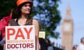 A young female junior doctor holds a board saying 'Pay restoration for doctors' on the picket line outside St Thomas' Hospital, London, on a sunny July 2, 2024.