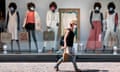 A woman in a mask walks by a store window of mannequins wearing masks