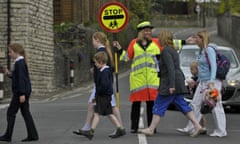 A lollipop lady helping primary school children to cross the road.